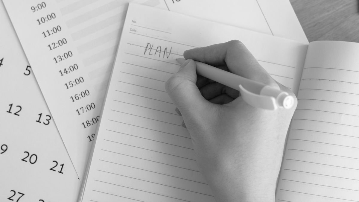Person planning weekly career goals in a notebook beside a laptop