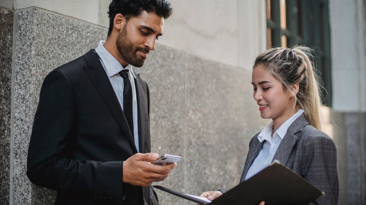 Two professionals talking while holding documents and a smartphone