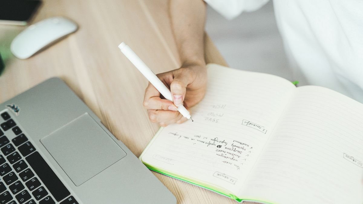 Person taking notes beside a laptop before writing a job application