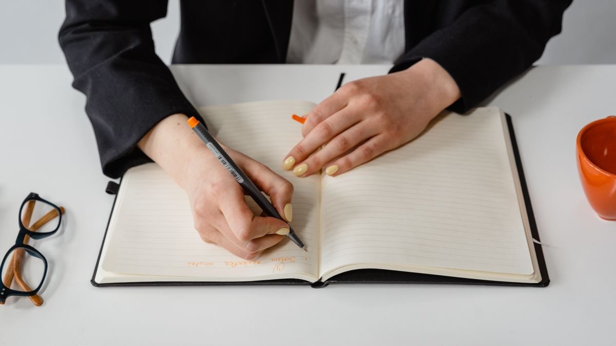 Person writing notes beside a laptop while organizing education details