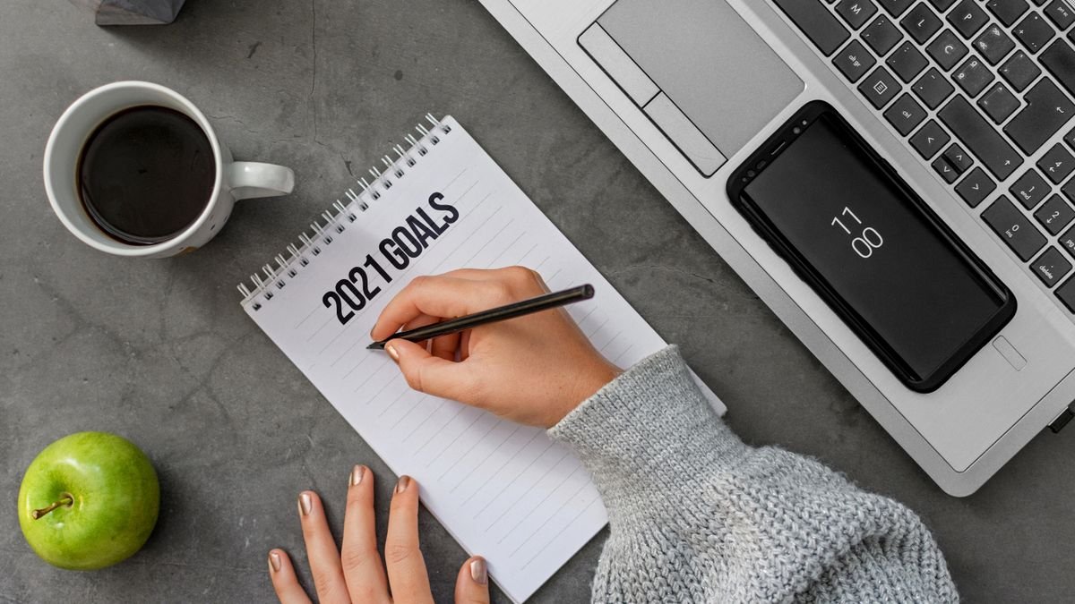 Person writing career goals in a notebook beside a laptop
