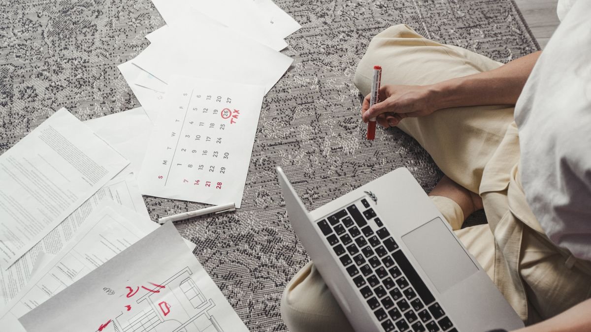 Person organizing job search tasks with documents, a calendar, and a laptop