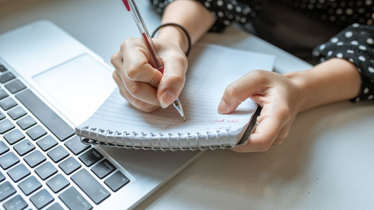 Person writing a learning plan beside a laptop
