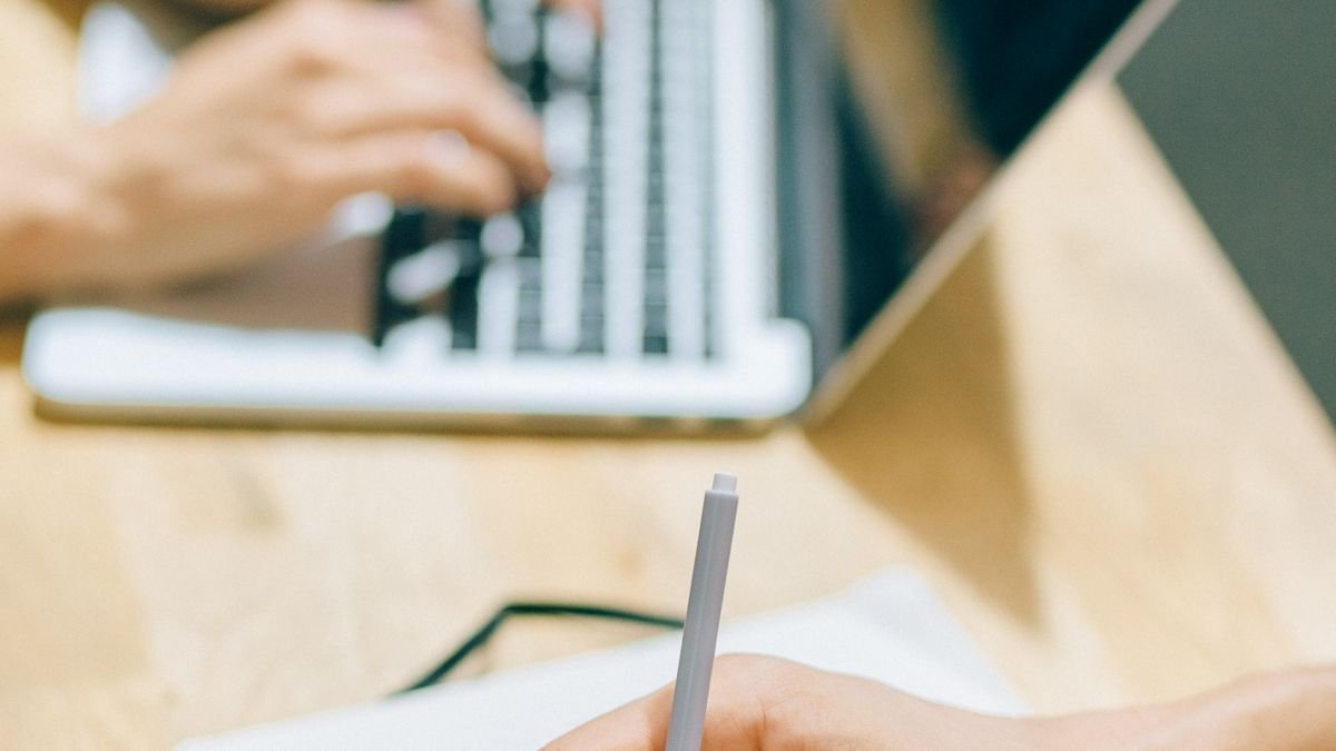 Two people collaborating with a laptop and notebook on a project
