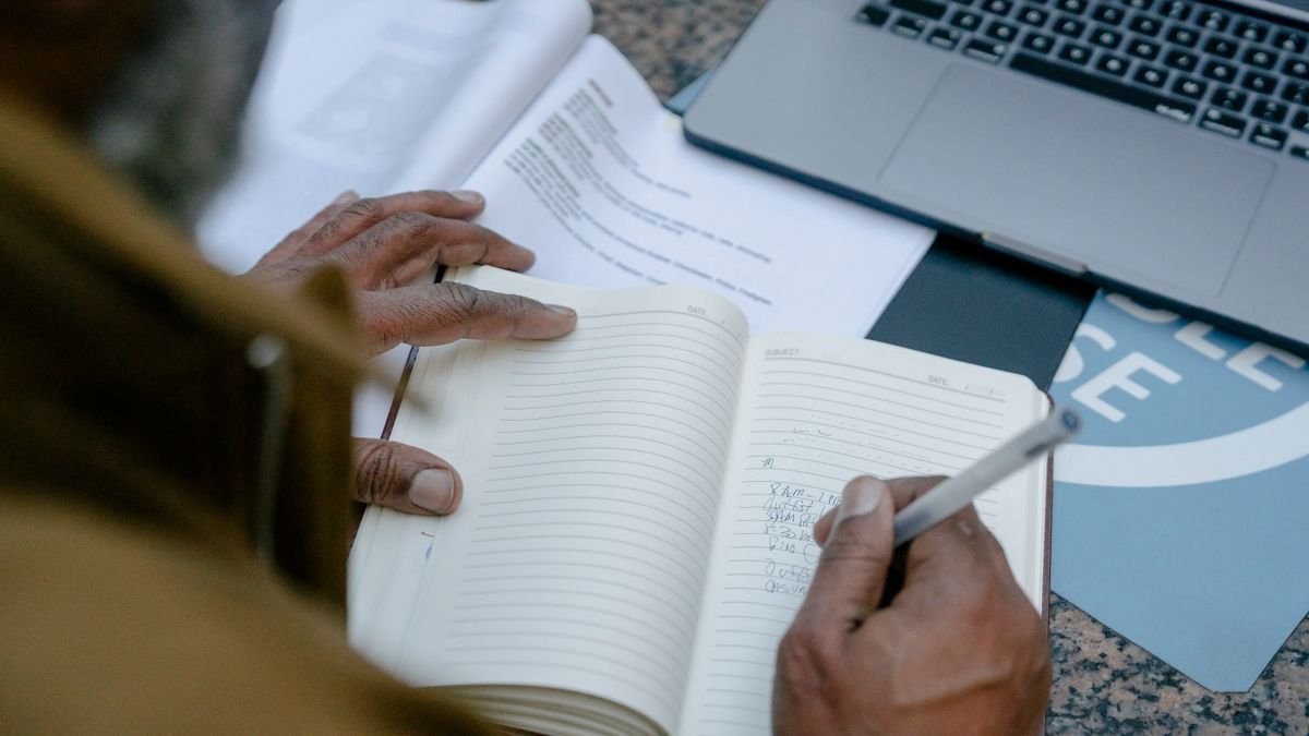 Person writing project notes beside an open laptop