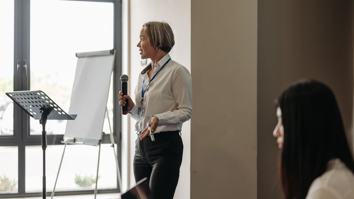 Professional woman speaking with a microphone beside a flipchart in a conference room