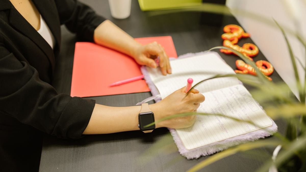 Professional writing a focused work plan in a notebook beside a laptop