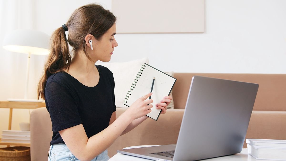 Learner attending an online class while taking notes on a laptop