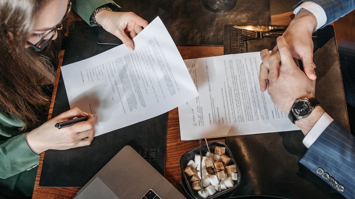 Professional reviewing and signing a job offer document beside a laptop