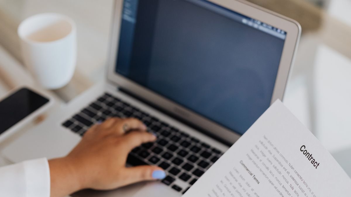 Person reviewing a contract beside a laptop before accepting an offer